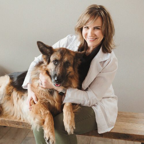 female veterinarian with should length brown hair posing with German Shepherd